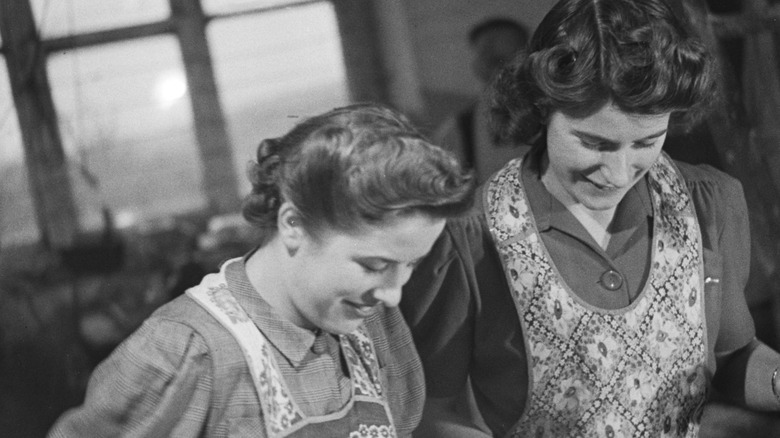 Two British young women wearing aprons in a kitchen.