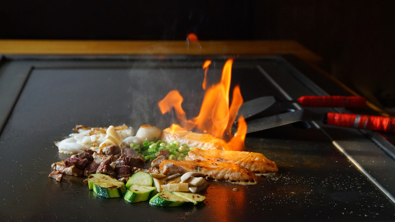 Vegetables, meat, and fish on a fiery flattop grill at a teppanyaki restaurant