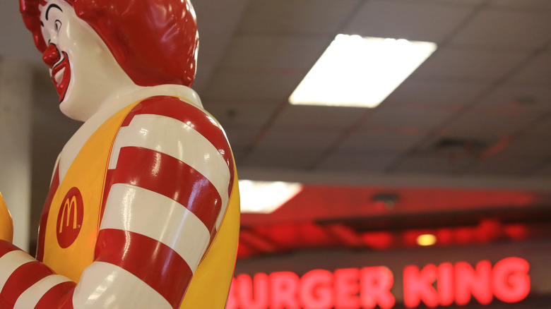 McDonald's mascot statue is posed in front of a Burger King sign