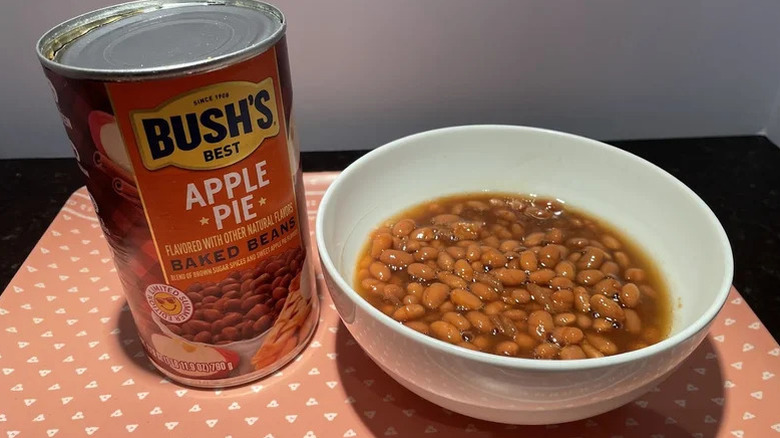 A can of Bush's Apple Pie Baked Beans next to a white bowl filled with the beans.