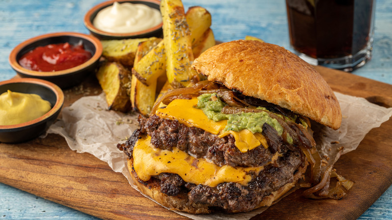 Double smashburger with cheese, caramelized onions on a wood cutting board with french fries and sauces