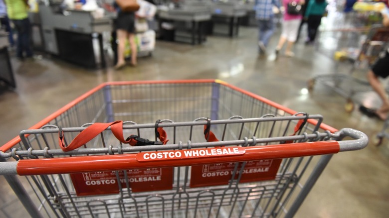 An empty Costco Wholesale cart inside of a busy Costco store by the checkout area.