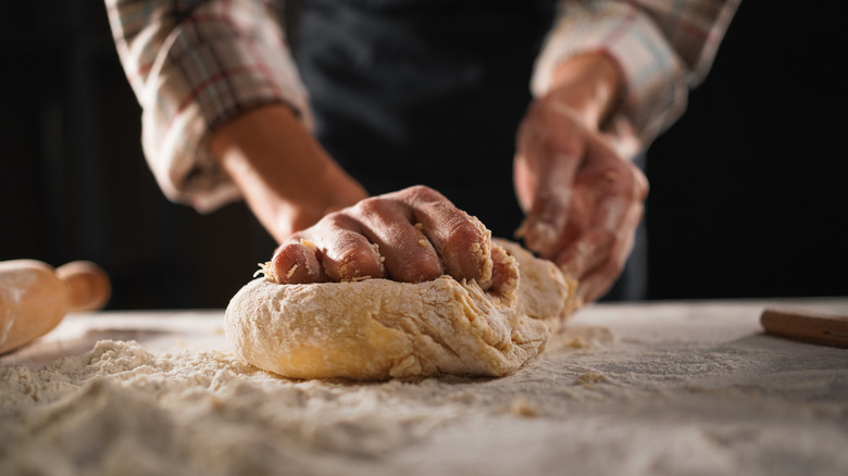 Hands knead dough on wooden table.