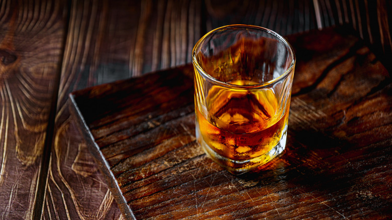 A glass of bourbon on a wooden tray