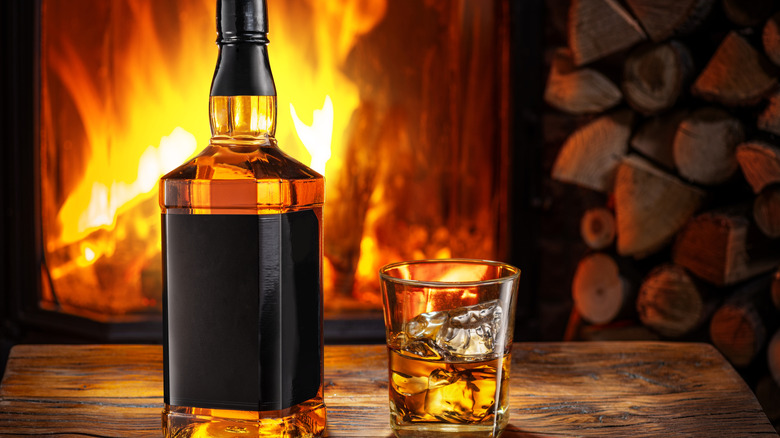 A bottle and a glass of bourbon set against a cozy fireplace