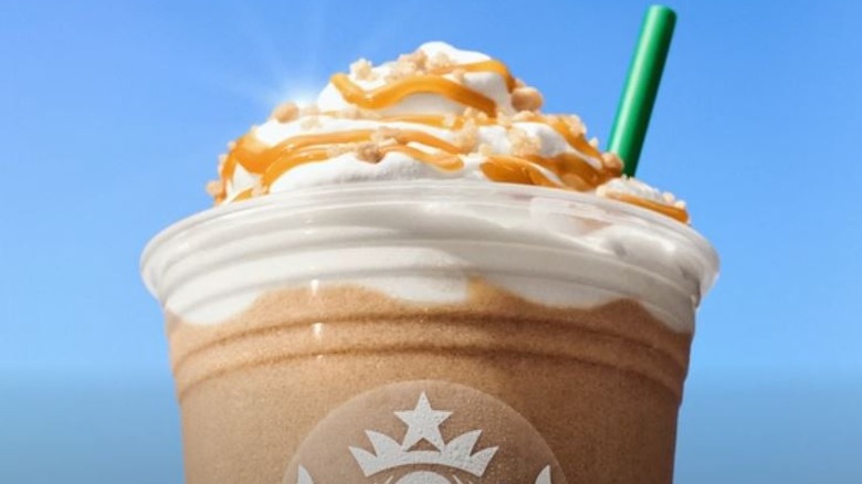 Close-up of the top of a caramel ribbon crunch Frappuccino in front of a blue sky.