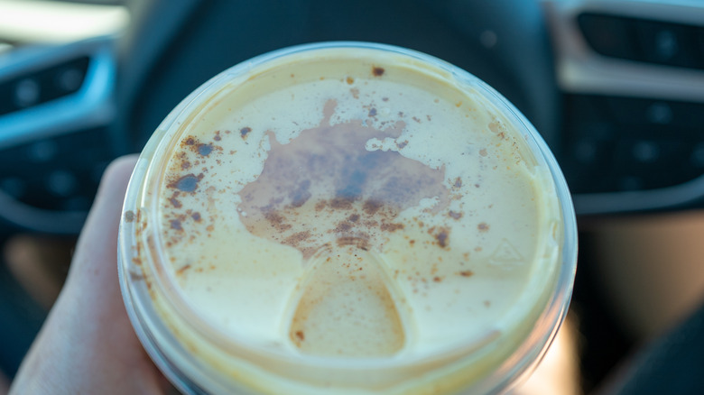 A hand holding a cold foam topped coffee drink with a clear lid