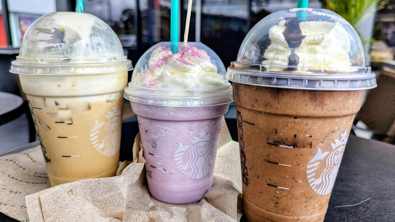 Three frozen Starbucks Frappuccinos in various colors and sizes on a table