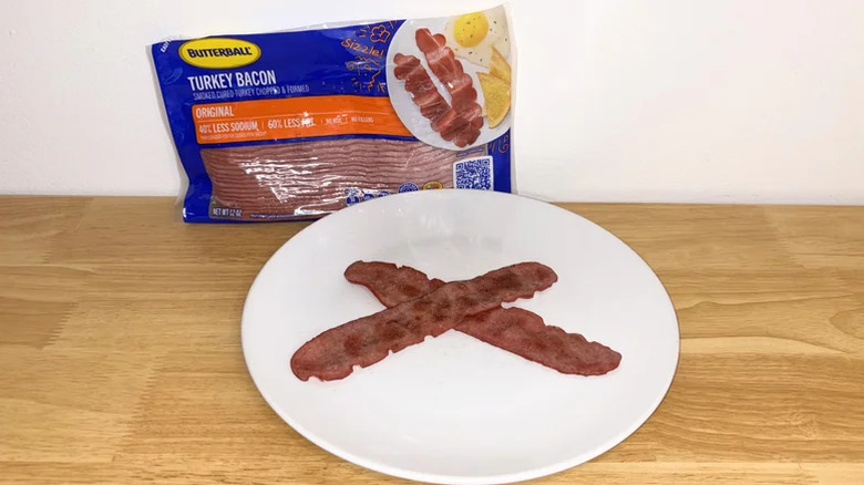 Two strips of cooked Butterball turkey bacon in front of a package of that bacon.