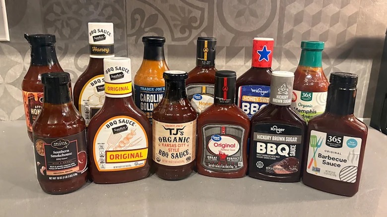 12 different bottles of store-bought grocery store sauce lined up on a white counter