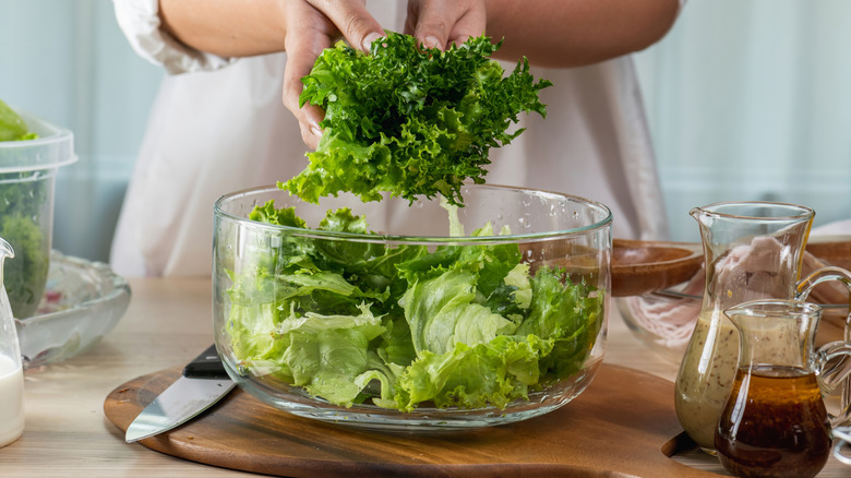 hands placing salad greens into clear glass bowl