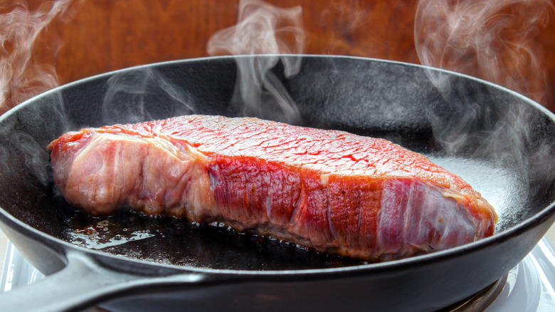 raw steak in a smoking-hot cast iron skillet