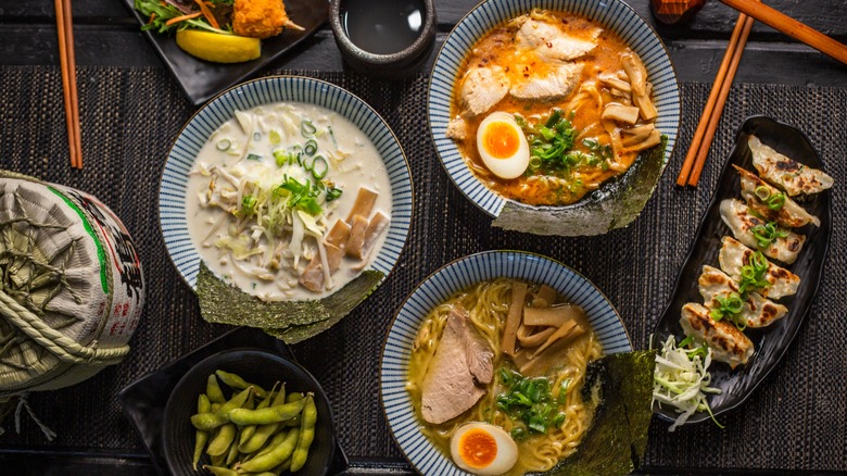 A table with three different kinds of ramen in bowls, with a side of gyoza dumplings