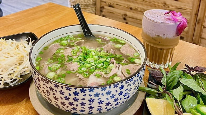 Bowl of pho, a plate of bean sprouts, and an iced coffee beverage on a table