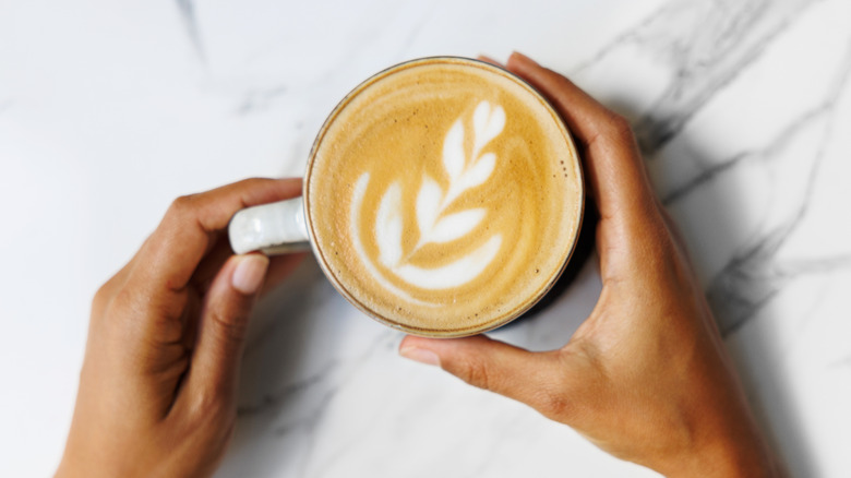 Hands holding a latte on a marble counter.