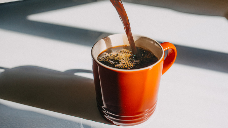 Pouring coffee into an orange-red mug