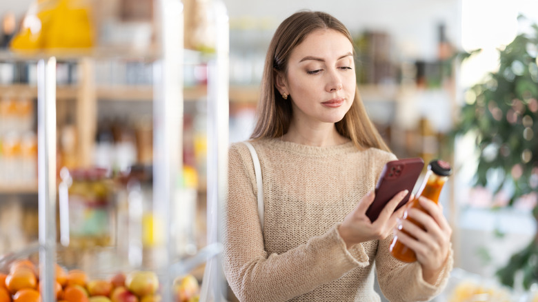 Young woman scans the label of a bottle with her phone in a grocery store