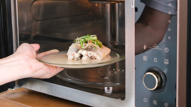 A person placing fish in a microwave for steaming