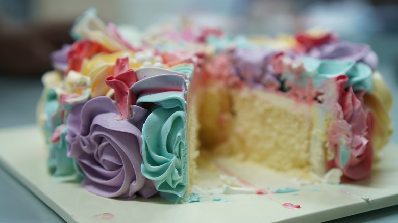 A small round cake with a slice removed is beautifully decorated with colorful frosting swirled into flower shapes