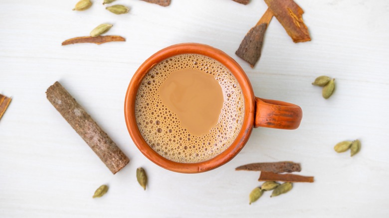 A cup of hot masala tea or masala chai in a clay cup with spices scattered around