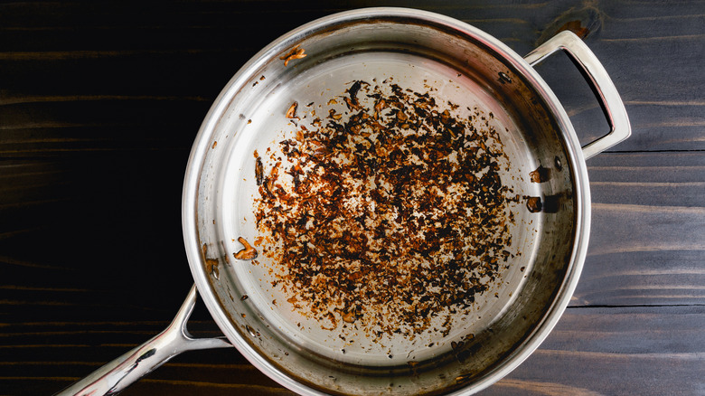Stainless steel pan on top of wood counter with burnt stuck on food inside.