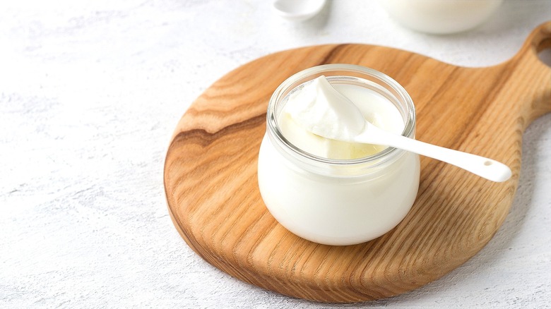 Yogurt in a small glass jar with a white spoon on a round wooden platter