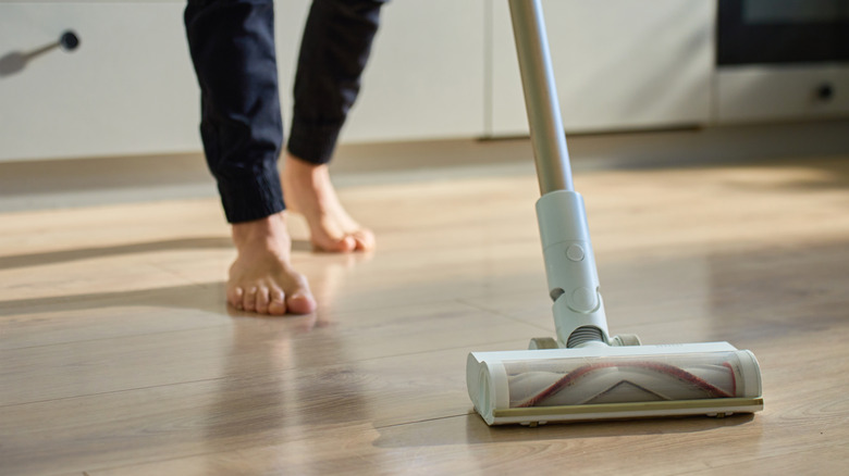 Someone barefoot vacuuming a kitchen floor with a stick vacuum