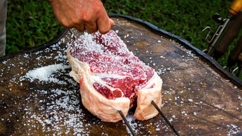 skewered steaks being salted before rotisserie grilling