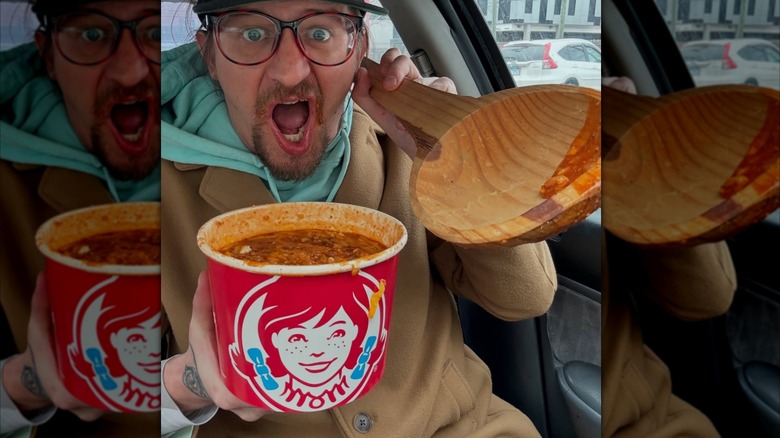 Someone poses with a bucket of chili with a giant wooden spoon