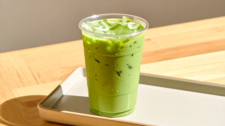 Iced matcha in a plastic cupon a wooden tray