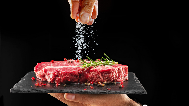 A hand salting a steak