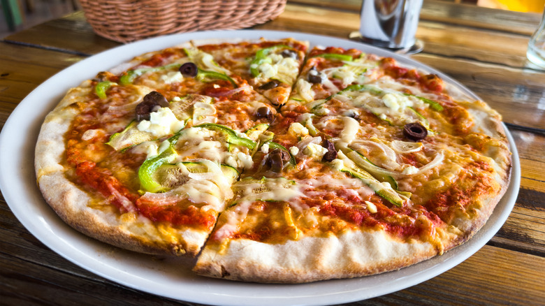 Thin crust pizza  with veggies on a white plate on a table