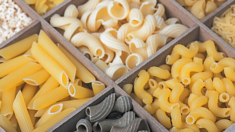 An assortment of pastas in different colors and shapes separated by wooden dividers.