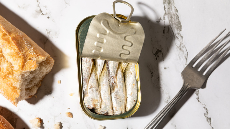 an open can of sardines and a baquette and fork on the side