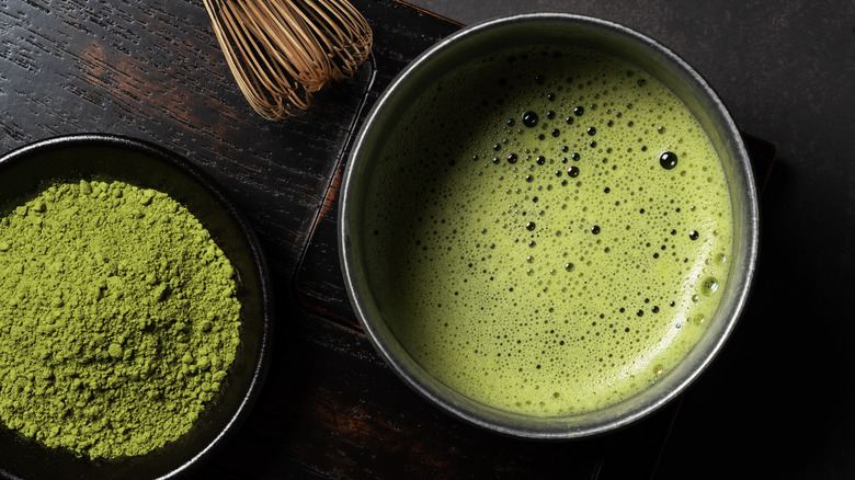 A bowl of bright, green matcha powder is pictured besided a frothy bowl of dissolved matcha.