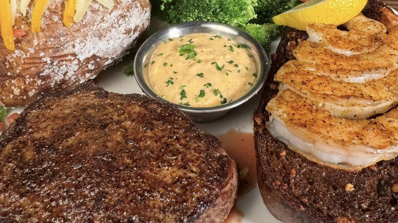 Two sirloins from Outback Steakhouse with grilled shrimp, broccoli, and a baked potato.