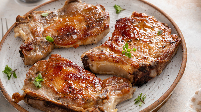 Cooked pork chops on a plate with herbs.