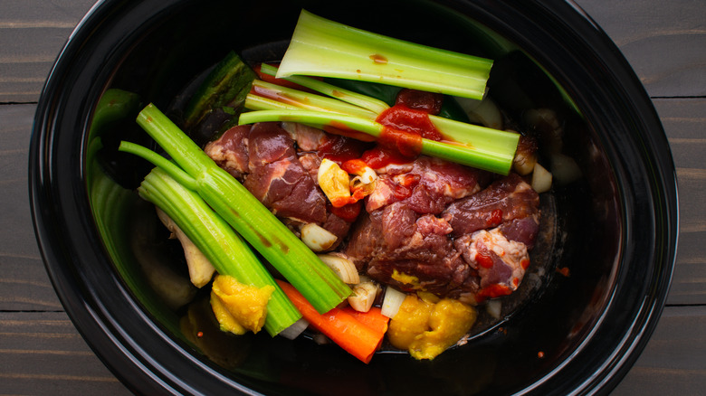 Pork shoulder with celery and carrots and aromatics in a slow cooker.