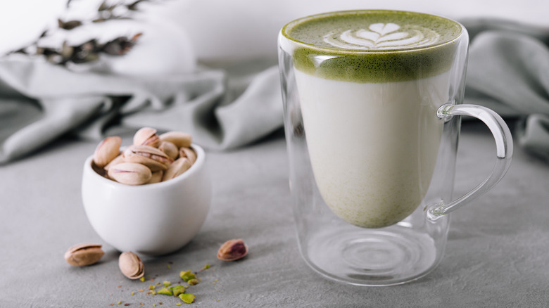 Cup of pistachio latte with pistachio nuts in a bowl beside it