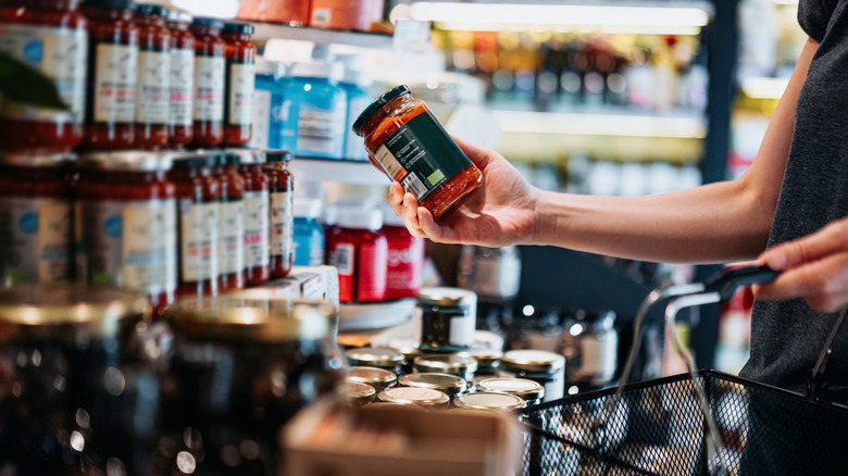 Person looking at jar of marinara sauce in supermarket