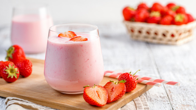 glass of pink strawberry milk surrounded by fresh strawberries