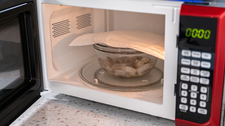 A bowl of shrimp covered with paper towel in the microwave