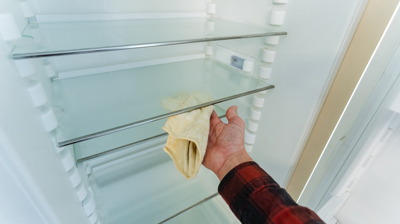 Person wiping down a refrigerator shelf with a cloth