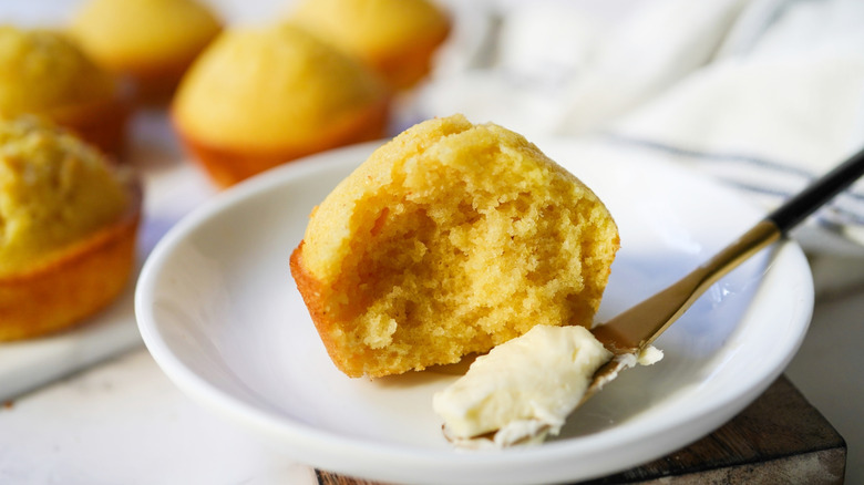 Partly eaten cornbread muffin next to butter knife with butter
