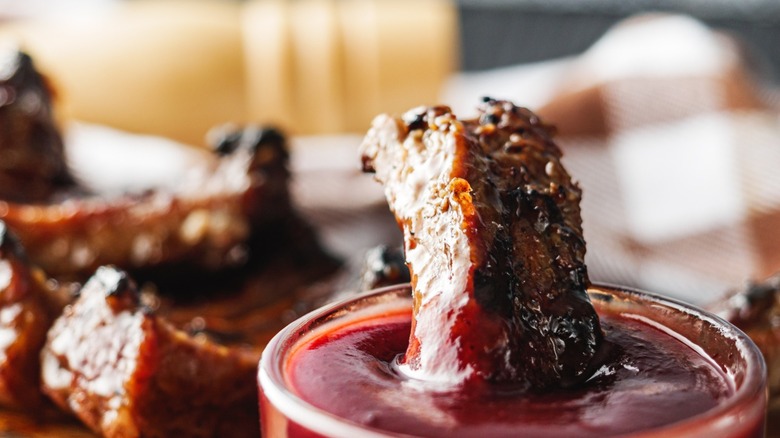 Barbecue pork being dipped in a small dish of BBQ sauce.