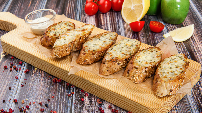 Toasted garlic bread topped with cheese on a wooden cutting board with a dip.