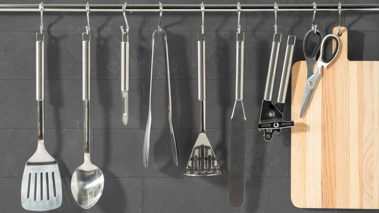 Kitchen utensils on a rail against a gray tile wall