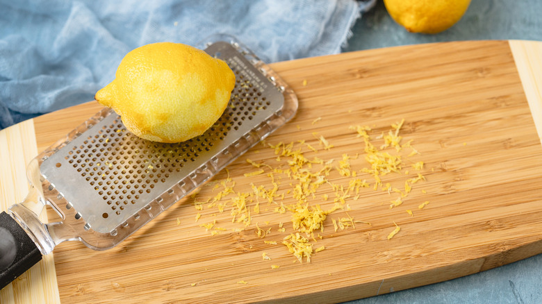 Microplane with fresh lemon making lemon zest on wooden board against a blue background