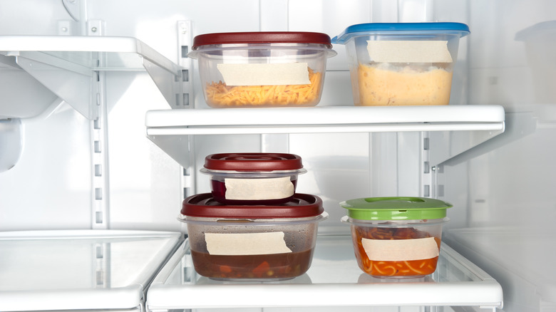 Unlabeled plastic containers filled with food and sitting on fridge shelves