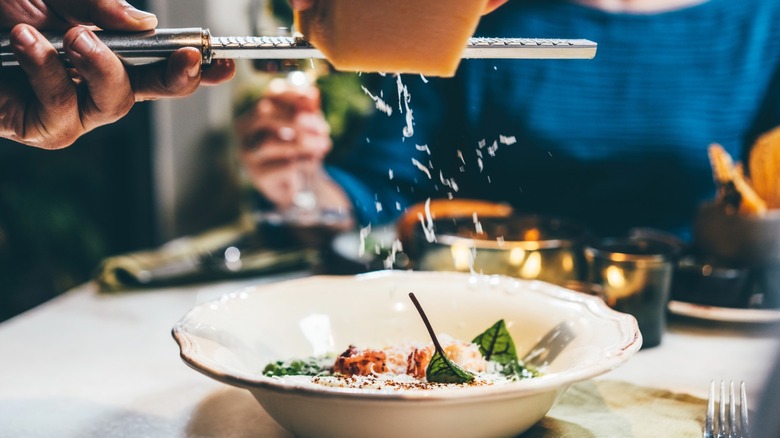 Person grating Parmesan over a bowl of risotto